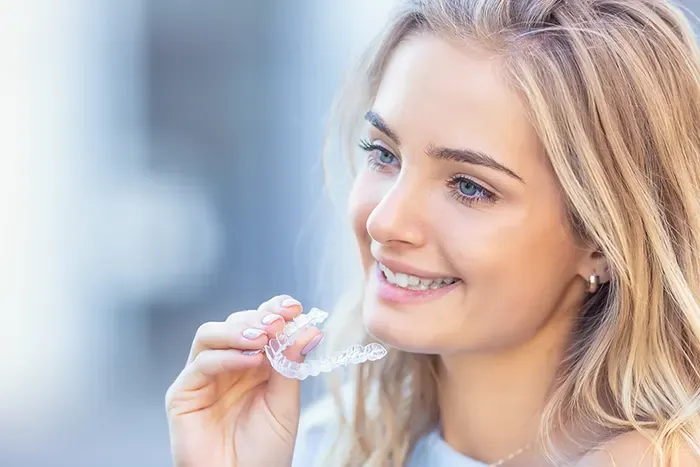A woman placing a clear Invisalign aligner over her teeth